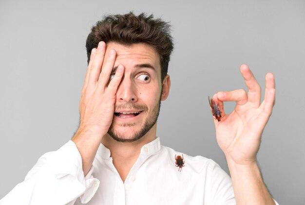 Man showing okay sign with one hand while covering one eye with the other, holding a small object between fingers